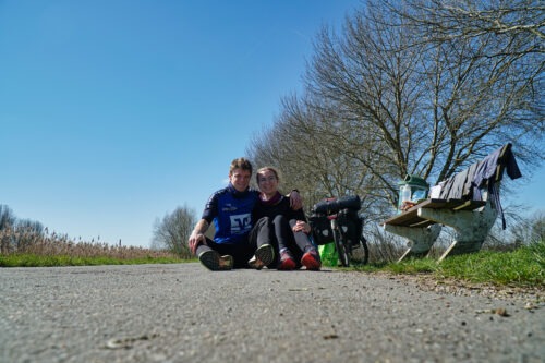 Charlotte und Yannik sitzend auf dem Fahrradweg in Belgien bei der Probetour im Frühjahr 2023